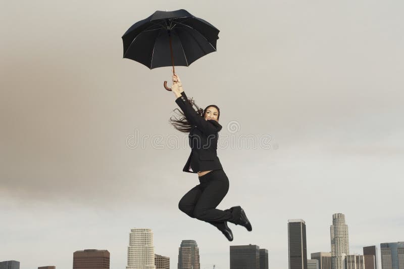 Businesswoman With An Umbrella Flying Above City. Full length of young businesswoman with an umbrella flying above city stock photos