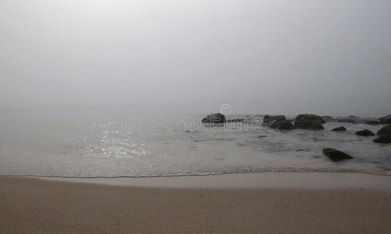 Fog in el arenal beach in mallorca. Rare and unusual heavy fog over the coast with sun umbrellas and shoreline with rocks at El Arenal beach touristic area royalty free stock images