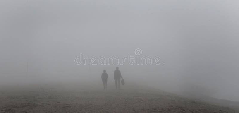 People walking on the beach under a heavy midday Fog covering el arenal beach in mallorca. Rare and unusual heavy fog over the coast with sun umbrellas and royalty free stock image