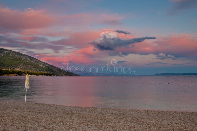 Stunning sunset on the sea. Pink, blue and white clouds with unusual shapes at sunset. On the pebbly beach is closed in the sun umbrella, the sea and a small stock image