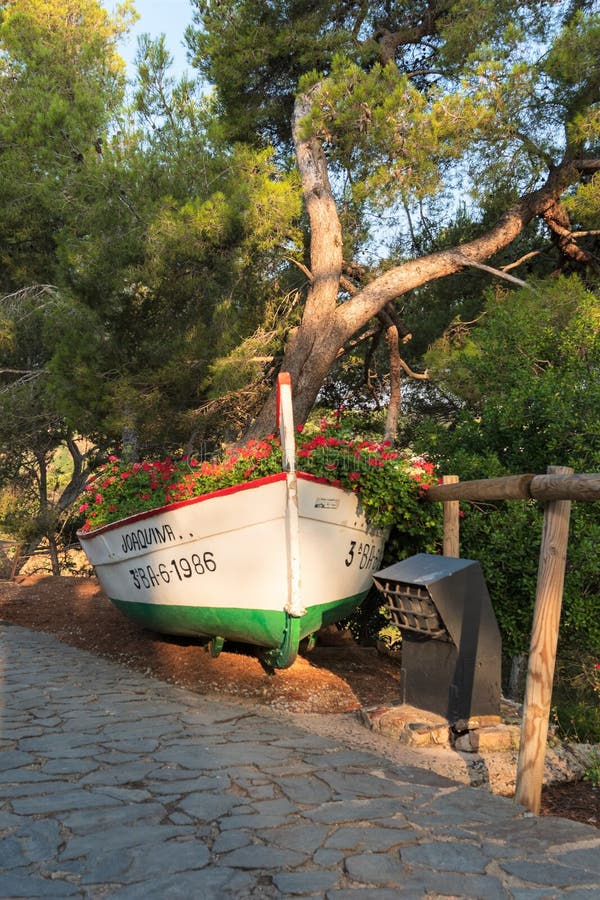 Tossa de Mar, Spain, August 2018. A boat used as a flowerbed in an old park. The original use of a vintage boat as an art object that draws attention to the stock photography