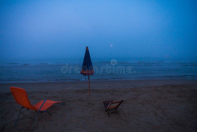 A view of an umbrella and two deckchairs on the beach during an unusual summer foggy morning.  stock photos