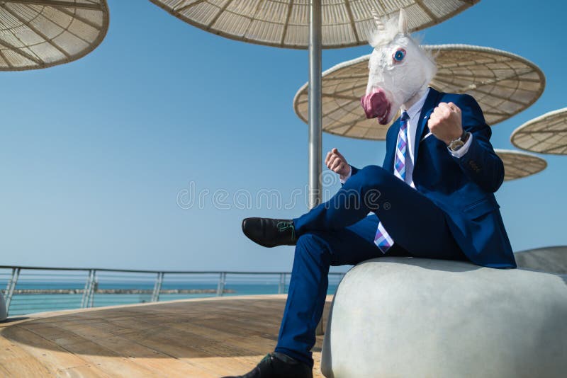 Young man in suit sits under umbrellas on the city waterfront and clenches fists. Young man in suit sits under umbrellas on the city waterfront and clenches his royalty free stock photography